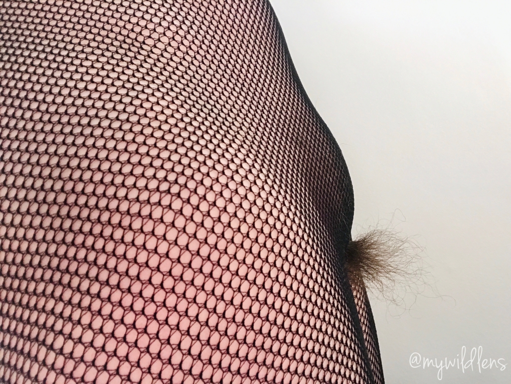 A view of the side of my body. I am wearing fishnet tights and nothing else, and my hair is spilling out of the gap at the crotch.